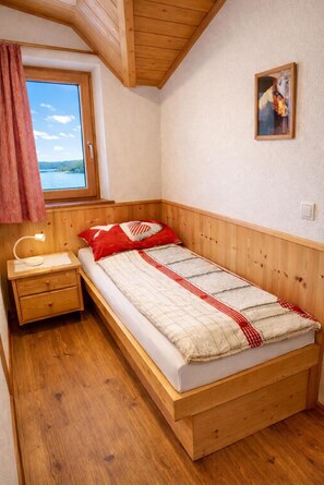 A small, cozy bedroom with a wooden bed, a nightstand, a window with a view of the outdoors, and a painting on the wall. - Apartment 'Binterhof Rosalpina Bio' with Mountain View, Balcony and Wi-Fi (Kastelruth)