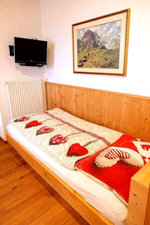 A single bed with a wooden headboard, a white mattress, and a red and white patterned blanket. - Apartment 'Binterhof Rosalpina Bio' with Mountain View, Balcony and Wi-Fi (Kastelruth)
