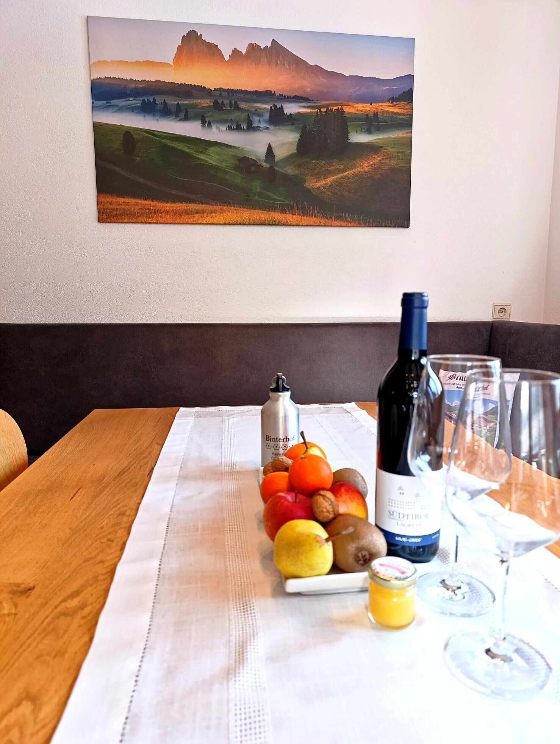A table with a bottle of wine, glasses, and a fruit arrangement.