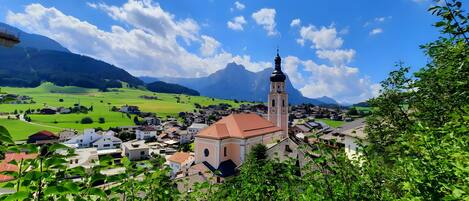 A town with a prominent church tower, surrounded by green fields and mountains.