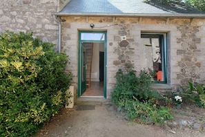 A stone building with a green door and window, a small garden with plants, and a number '2' sign on the wall. - Cottage 'Maisonnette du Paradis' (Pommerit-le-Vicomte)