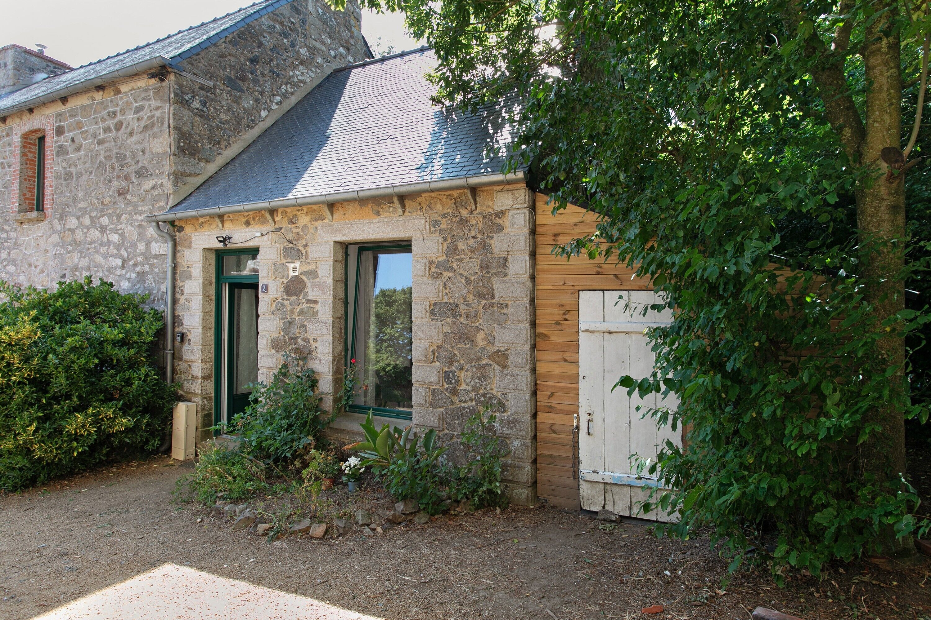 A stone building with a wooden door, a small porch, and a garden area.