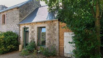 A stone building with a wooden door, a small porch, and a garden area.