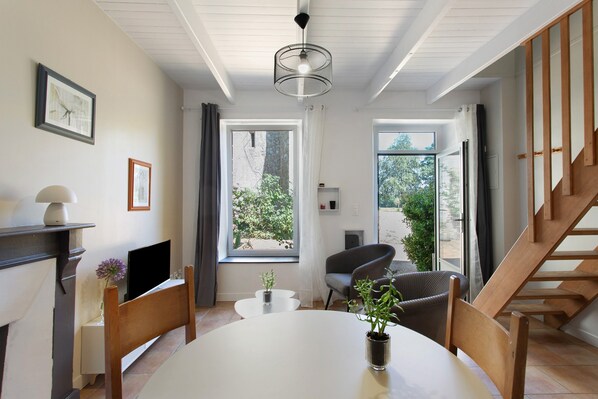 A modern living room with a dining table, chairs, a TV, and a staircase.