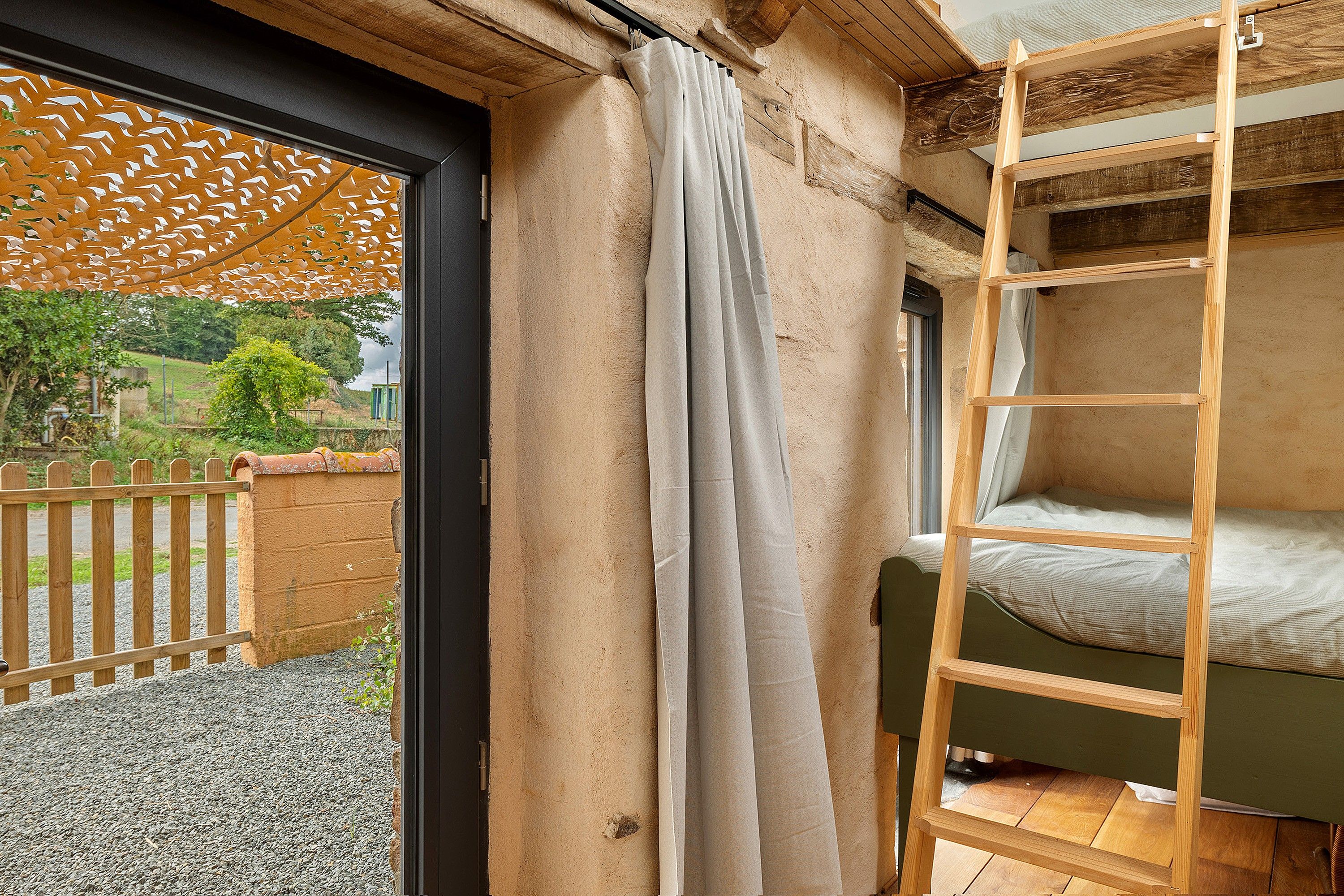 Une chambre avec un lit superposé, une fenêtre avec un rideau et une vue sur l’extérieur.