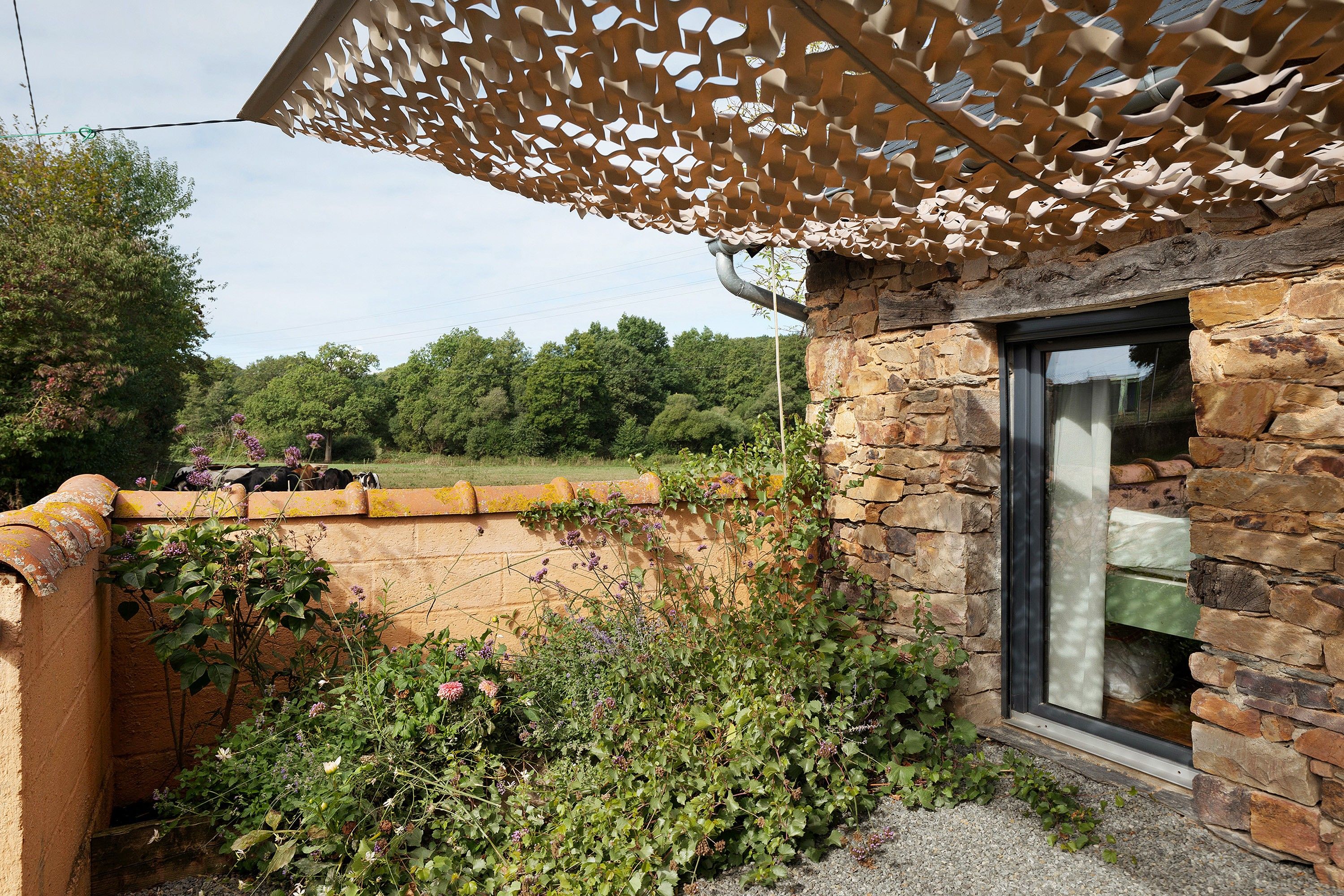 Un bâtiment en pierre doté d’une porte en verre, d’une clôture en métal et d’une pergola à structure ajourée.