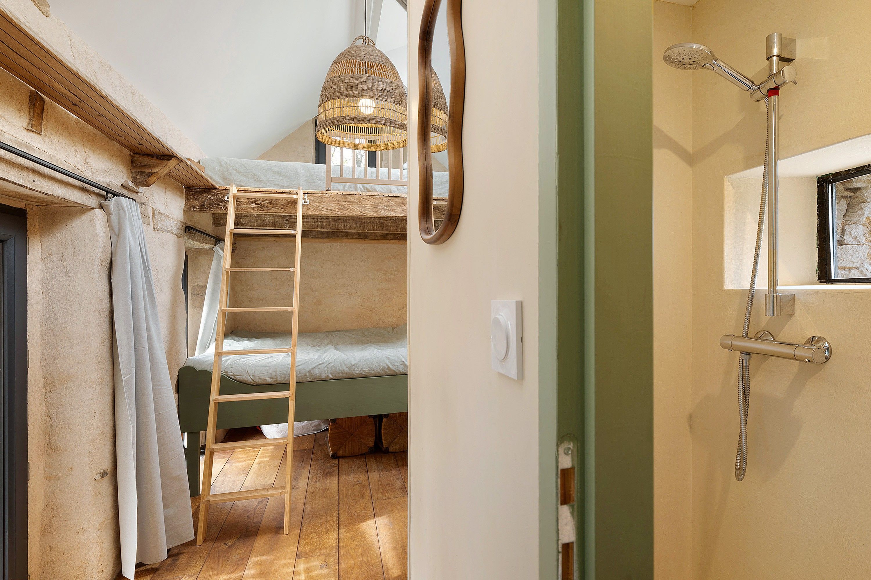 Een kamer met een stapelbed, een ladder, een hanglamp en een douche met een handdouche.