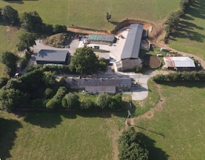 An aerial view of a property with multiple buildings, including a large central structure with a flat roof, surrounded by smaller buildings and open grassy areas.