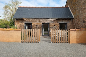 A stone building with a dark tiled roof, a wooden gate, and a gravel driveway.
