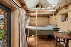 Une chambre de style « loft » avec un lit superposé, une échelle en bois, une table avec des chaises et une fenêtre avec des rideaux.