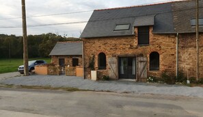 A stone building with a gravel driveway, a wooden gate, and a parked car.