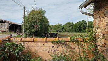 Un paysage rural avec un mur de pierres, un bâtiment en bois et une zone clôturée où se trouvent des vaches.