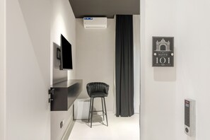 Una camera d'albergo moderna con una TV a schermo piatto montata a parete, una sedia nera, una tenda nera e un cartello con il numero della stanza 101.