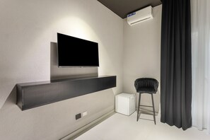 A modern living room with a flat-screen TV mounted on a wall, a black sofa, a small white side table, and a black curtain. - Bed and Breakfast 'Vicolo Del Fortino - Suite 101' with Balcony, Wi-Fi and Air Conditioning (Catania)