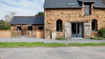 A stone building with a dark roof, a wooden fence, and a gravel driveway.