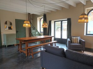 A spacious living area with a wooden table, benches, a sofa, and two hanging lamps.