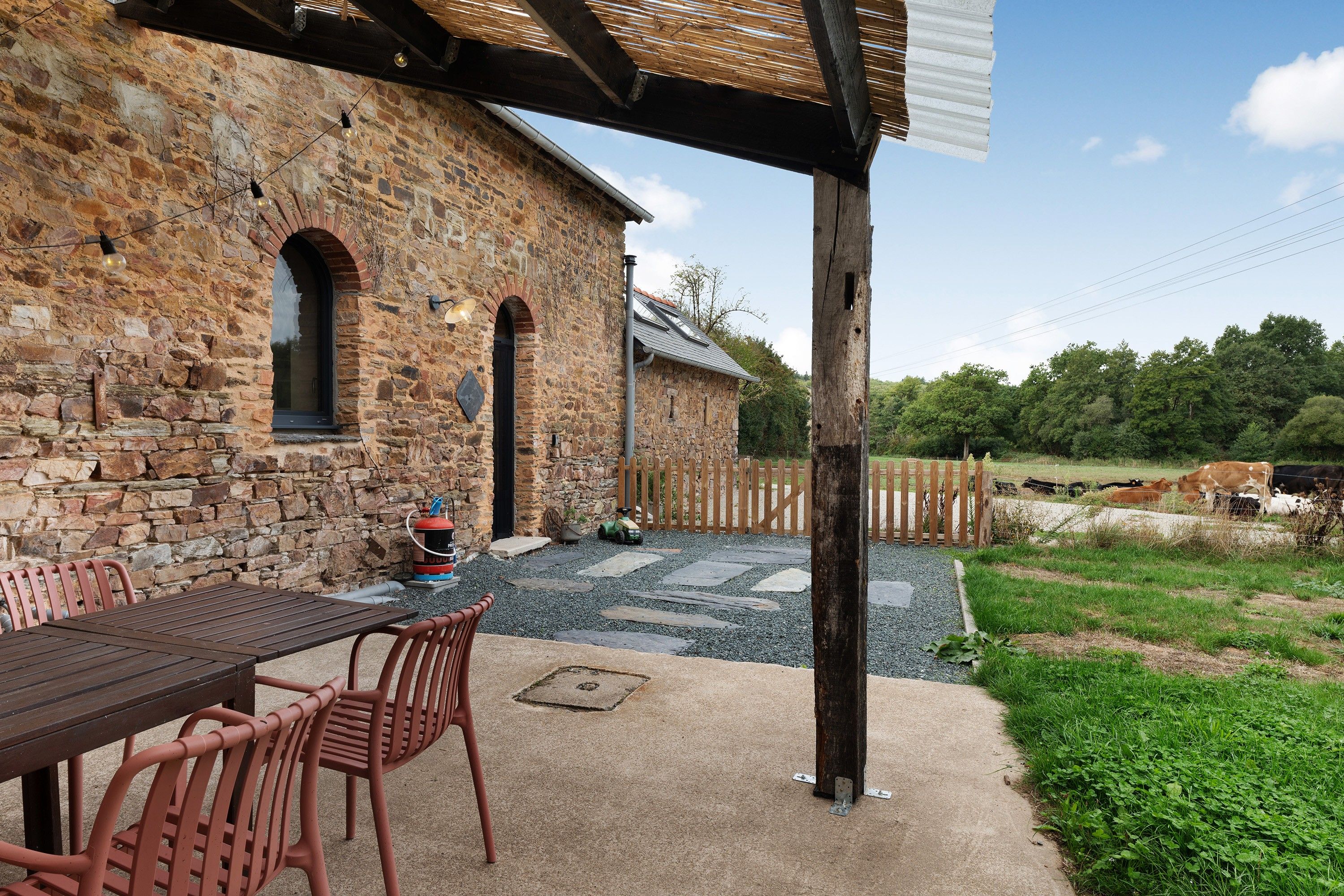 Un bâtiment en pierre doté d’un patio comprenant une table et des chaises, un extincteur et une clôture en bois.