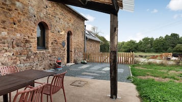 Un bâtiment en pierre doté d’un patio comprenant une table et des chaises, un extincteur et une clôture en bois.