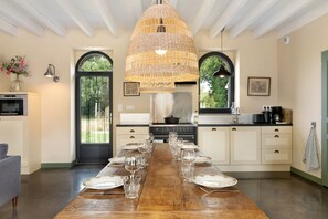 A dining area with a long wooden table set for a meal, kitchen appliances, and a large woven light fixture.