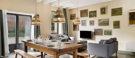 A dining area with a wooden table set for four, a grey sofa, and a TV mounted on the wall.