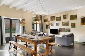 A dining area with a wooden table set for four, a grey sofa, and a TV mounted on the wall.