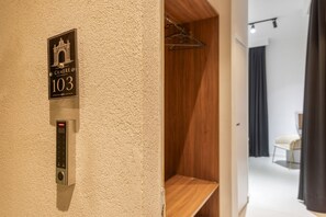 Ein Hotelzimmer-Eingangsbereich mit Klingel, einem Schild mit der Nummer 103 und einem Blick auf eine Holzwand sowie einen Stuhl im Hintergrund.