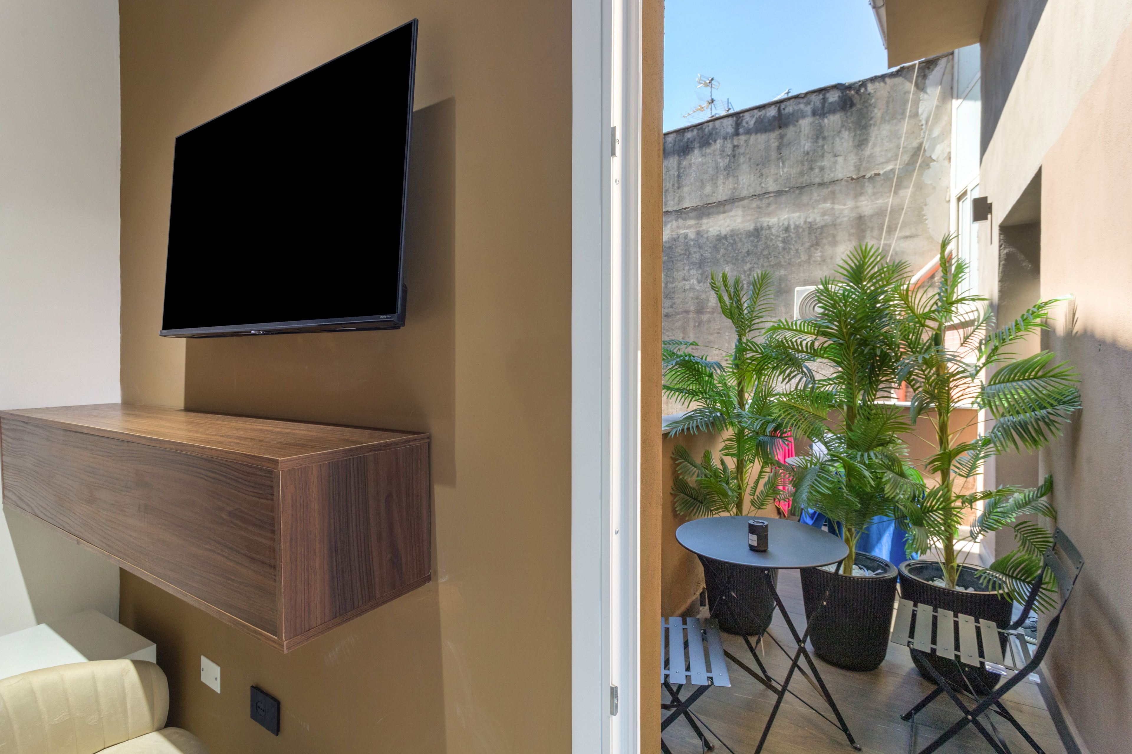 A modern living space with a mounted TV, a wooden cabinet, a small round table, and potted plants.