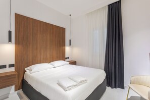 Ein modernes Hotelzimmer mit einem großen Bett, zwei Nachttischen, einem Sessel und einem großen Fenster mit Vorhängen.