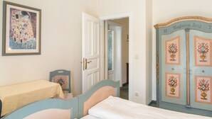 Ein Schlafzimmer mit einem Bett, einem Nachttisch, einem Sessel, einer Tür und einer Wand mit einem gerahmten Bild.