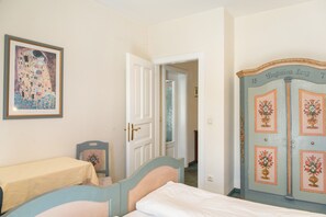 Ein Schlafzimmer mit einem Bett, einem Nachttisch, einem Sessel, einer Tür und einer Wand mit einem gerahmten Bild.