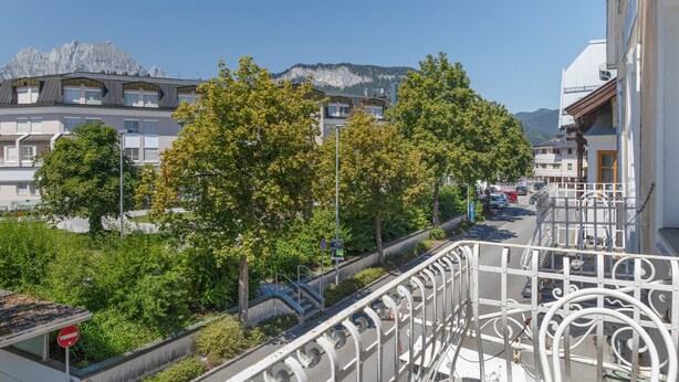 Ein Balkon mit Blick auf einen Berg, Bäume und eine Straße mit parkenden Autos.