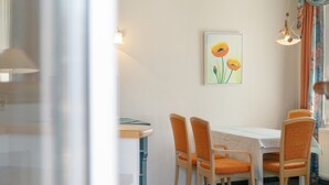 Ein Essbereich mit Tisch und vier Stühlen, einem Bild an der Wand und einem Fenster mit Vorhängen.