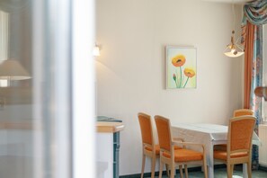 Ein Essbereich mit Tisch und vier Stühlen, einem Bild an der Wand und einem Fenster mit Vorhängen.