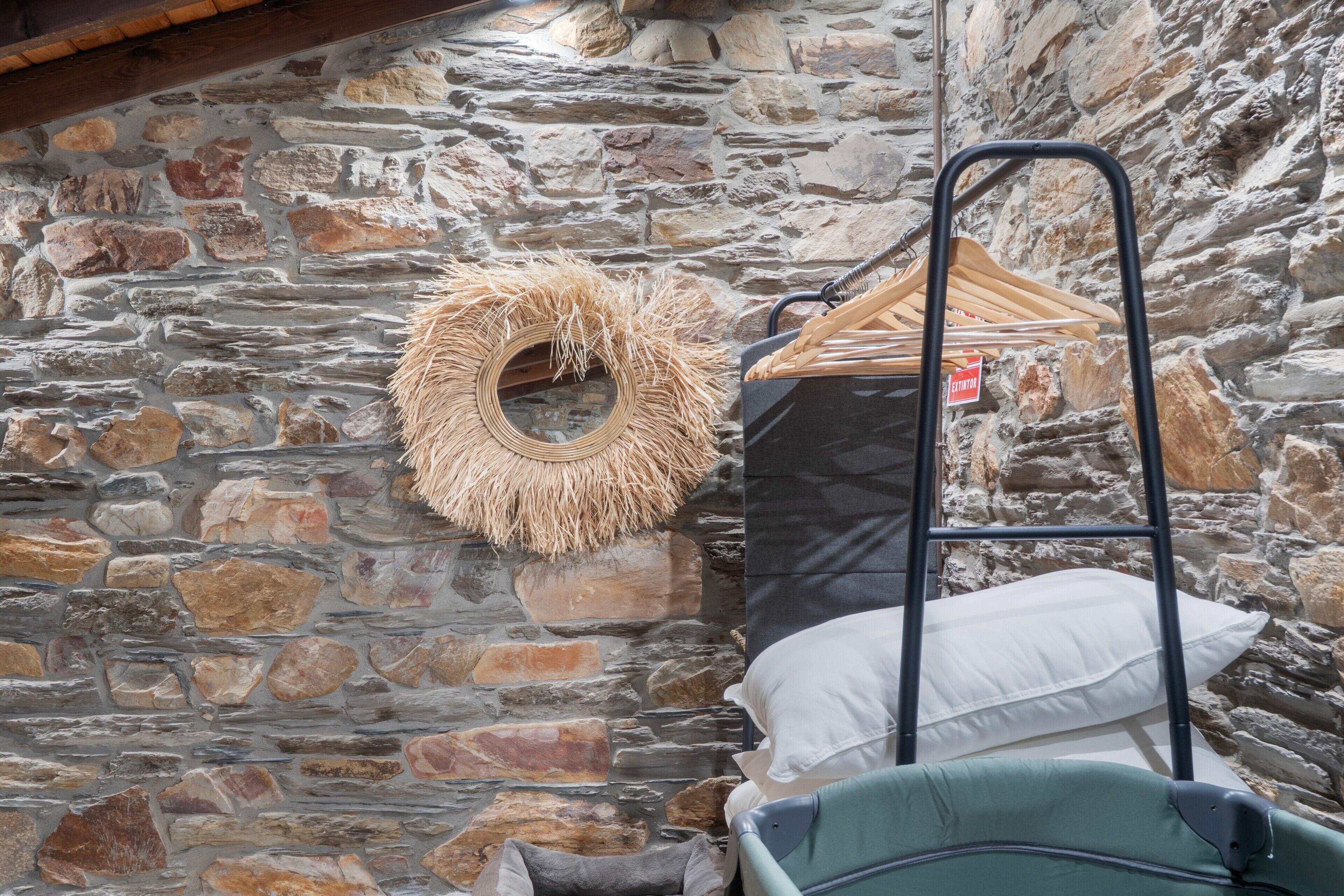 A stone wall with a circular woven item and a metal hanger rack with clothes.