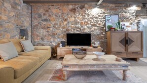 Una sala de estar con pared de piedra, techo de madera, un sofá, una mesa de centro y un televisor.