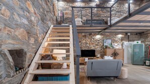 Un interior con varios niveles, una escalera de madera, un sofá, un televisor y un refrigerador.