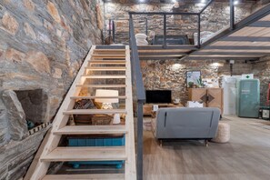 A multi-level interior with a wooden staircase, a sofa, a television, and a refrigerator.