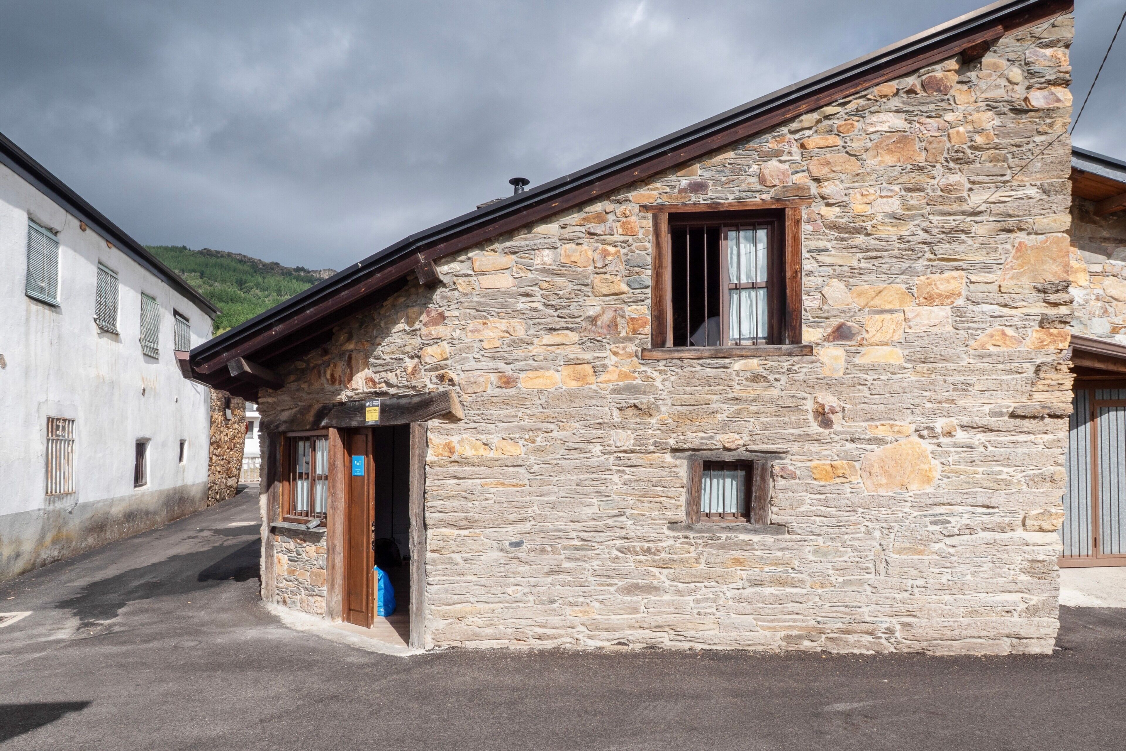 Un edificio de piedra con techo inclinado, una puerta de madera y un ventanal pequeño.