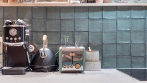Una encimera de cocina con cafetera, hervidor, tostadora y un tarro de azúcar.