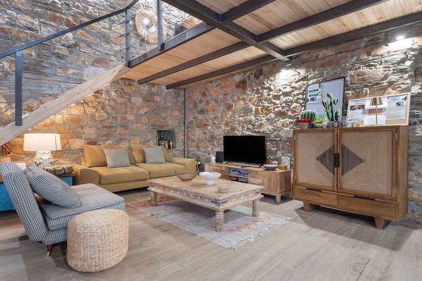 Una sala rústica con una pared de piedra, una escalera de madera, un sofá, un televisor y un aparador.