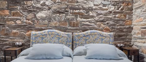 A double bed with a patterned headboard and pillows, set against a stone wall.