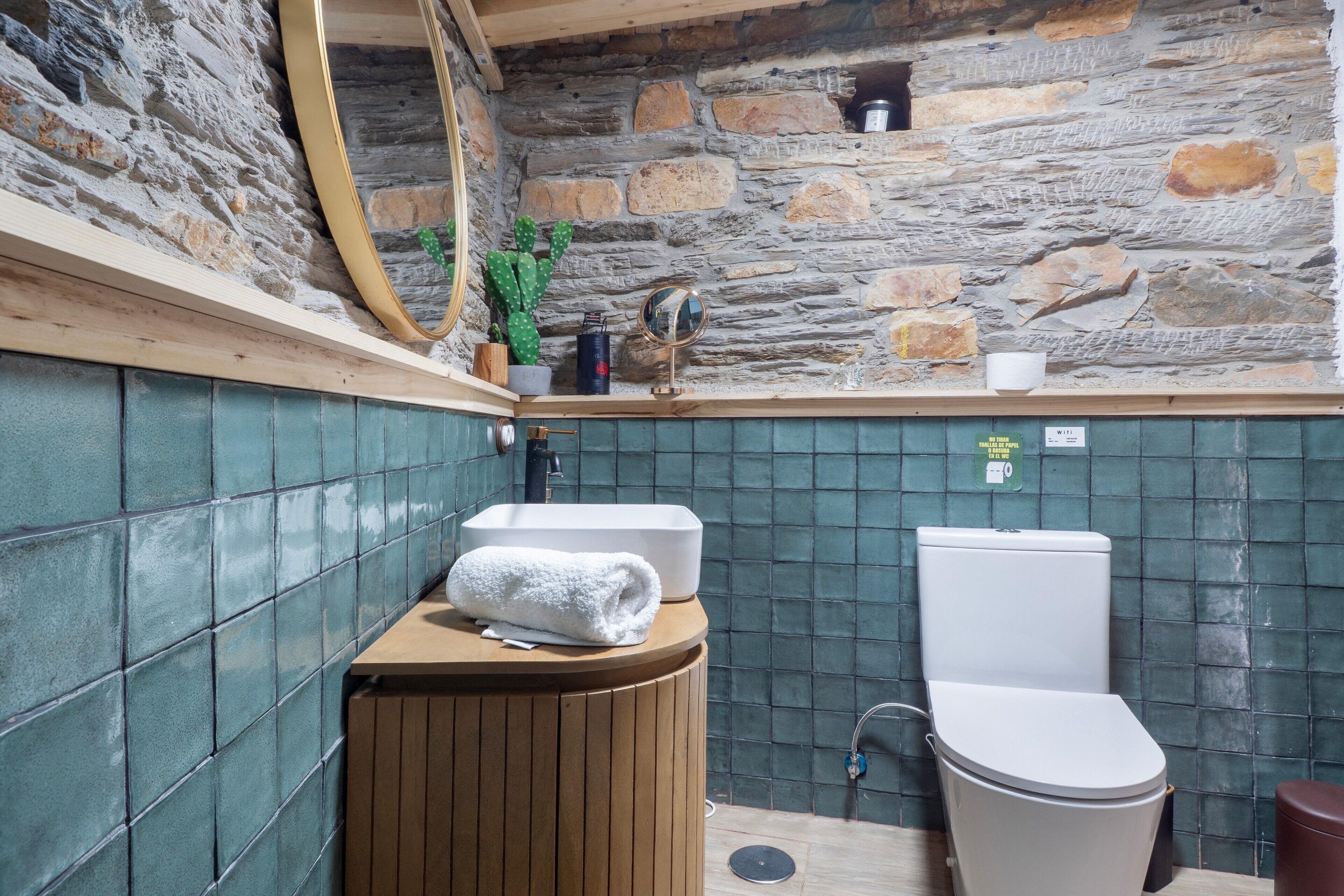 A bathroom with a stone wall, a sink, a toilet, and a mirror.