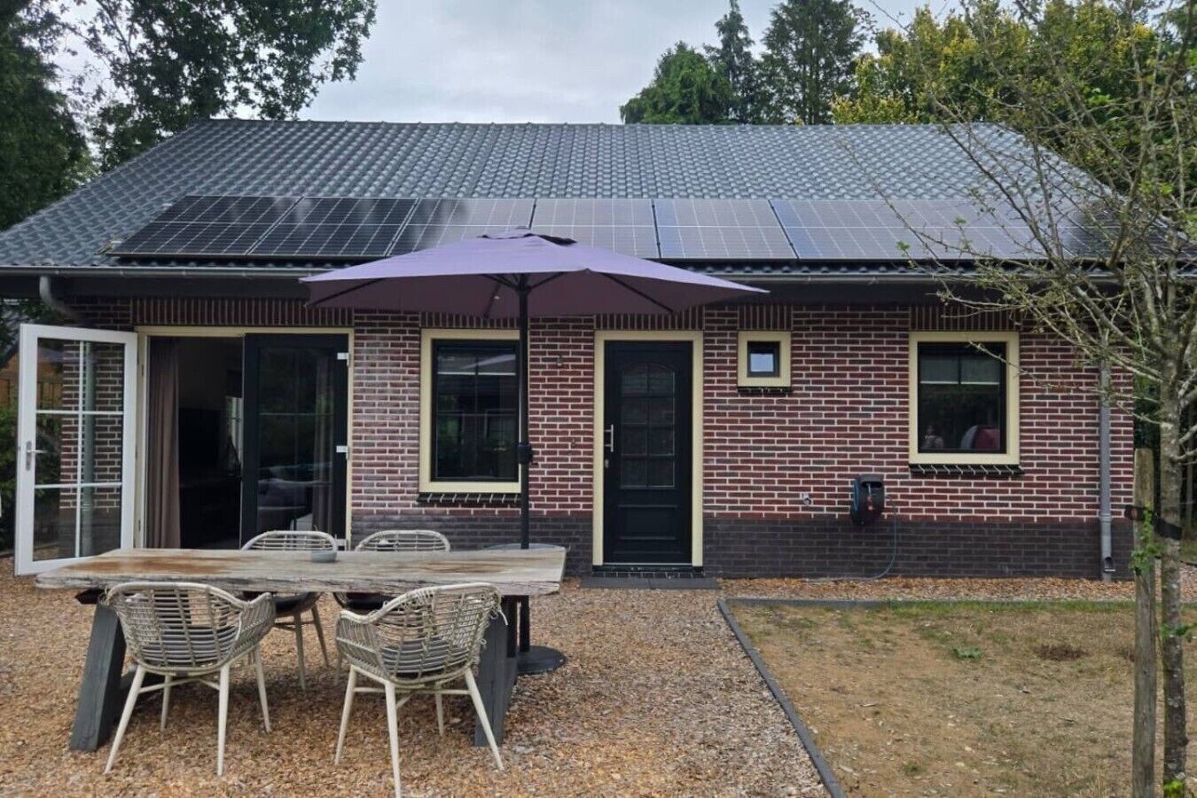Una casa in mattoni con tetto in tegole, un patio con tavolo e sedie, e un impianto di pannelli solari.