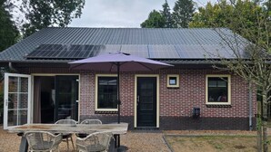 A brick house with a tiled roof, a patio with a table and chairs, and a solar panel array. - Eendje 1 | Vrijstaande 6-persoons vakantiewoning (Ermelo)