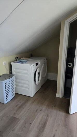 A laundry room with a washing machine and dryer, a laundry basket, and a door leading to another room. - Eendje 1 | Vrijstaande 6-persoons vakantiewoning (Ermelo)