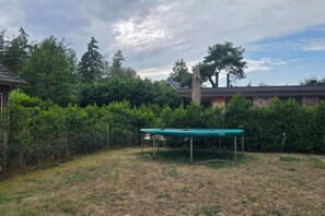 A backyard with a trampoline, dense shrubbery, and a house in the background. - Eendje 1 | Vrijstaande 6-persoons vakantiewoning (Ermelo)