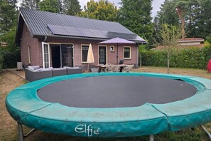 Una proprietà residenziale con una casa in mattoni, un trampolino e un patio con mobili da esterno.