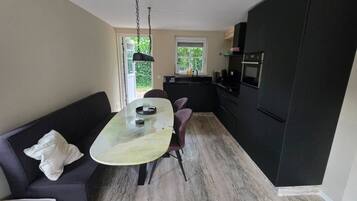 Una cucina compatta con zona pranzo, un divano nero e una finestra che lascia entrare luce naturale.