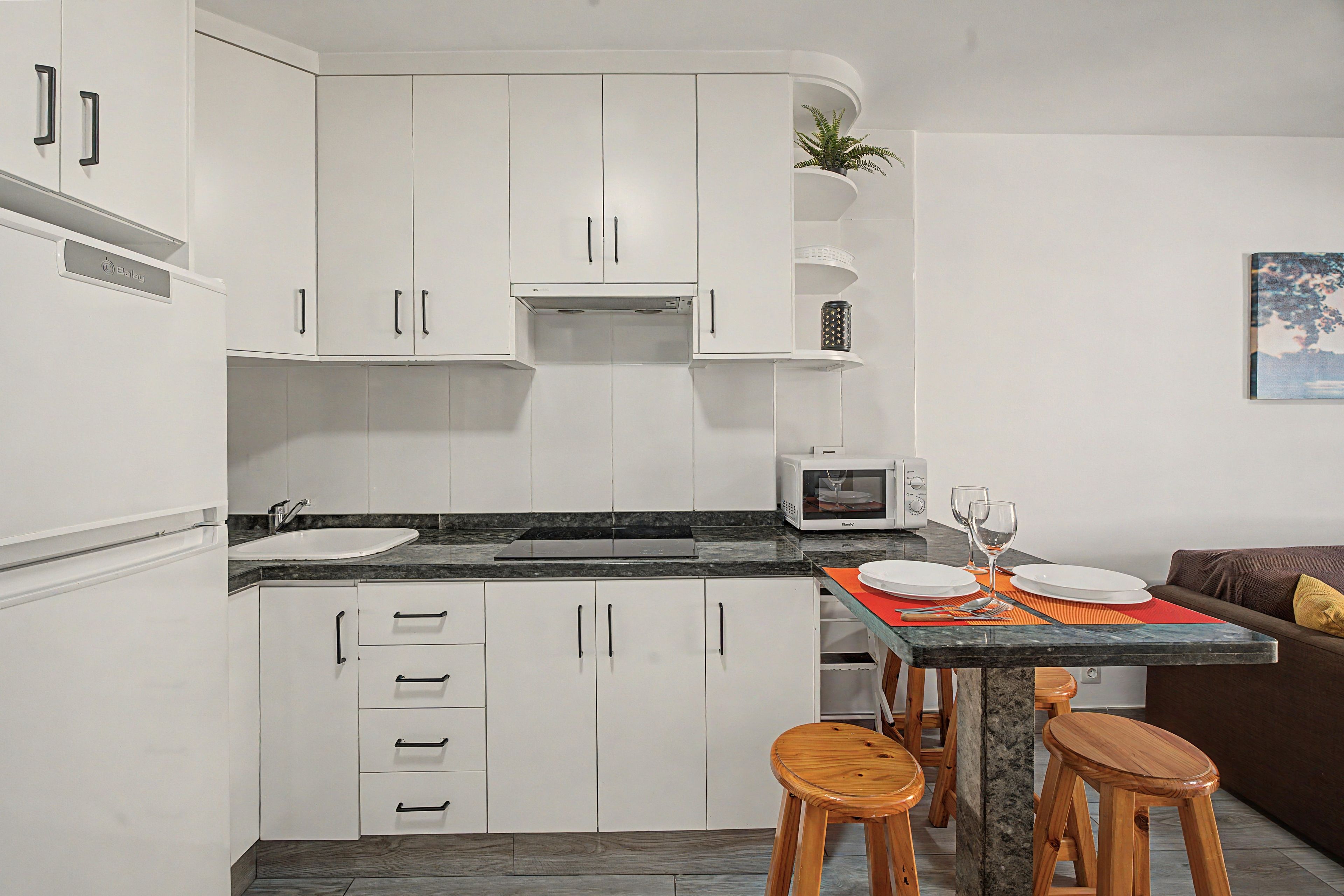 A compact kitchen with white cabinets, a microwave, and a dining area with stools.