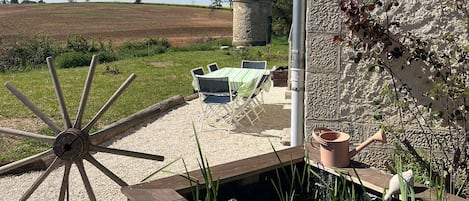 A rustic outdoor seating area with a wooden table and chairs, a decorative metal pole, and a stone wall with a metal sign.